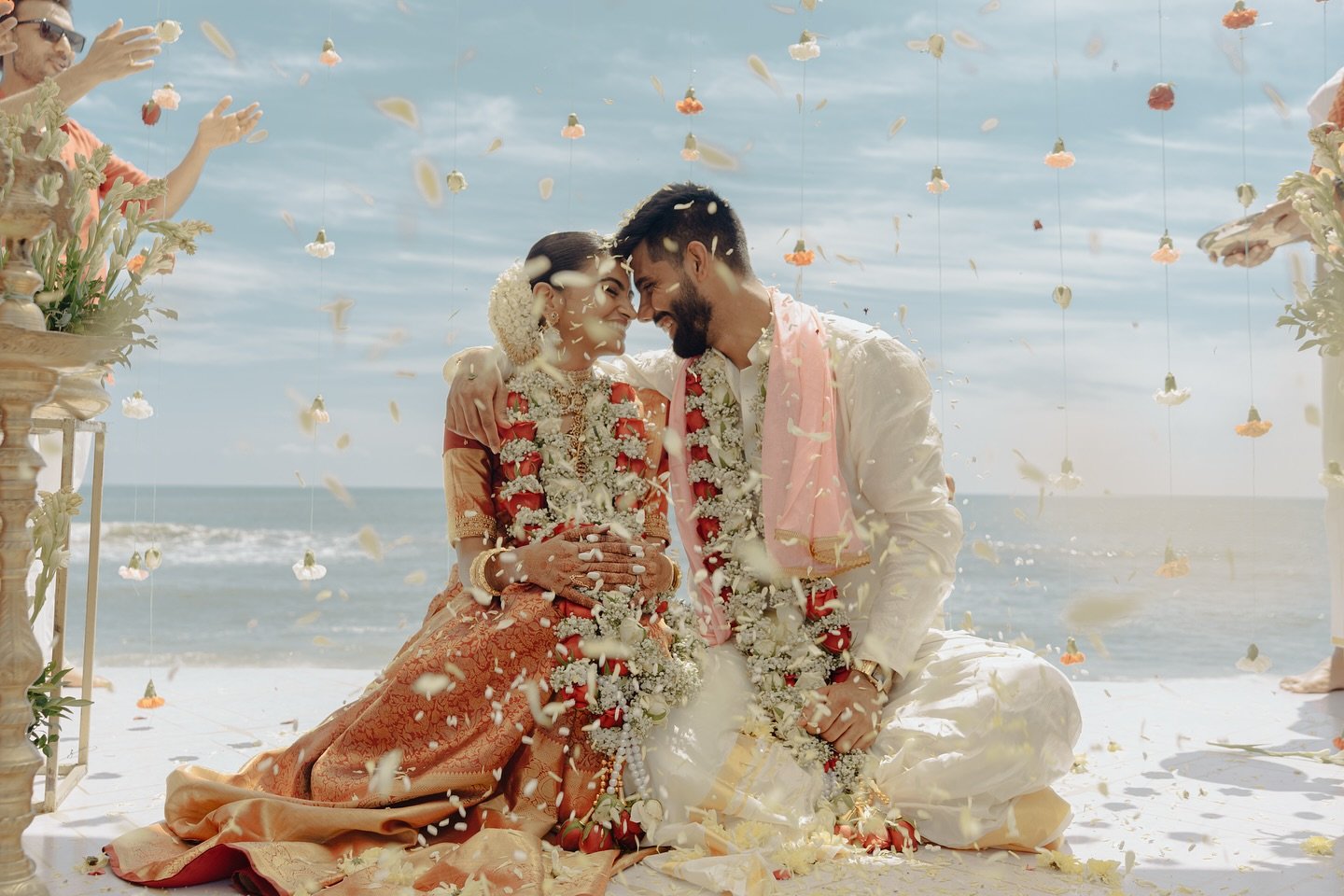 A newlywed couple smiling at one another beside the sea